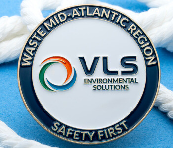 A circular enamel challenge coin for VLS Environmental Solutions Waste Mid-Atlantic Region featuring the text Safety First and a multi-colored swirl logo.