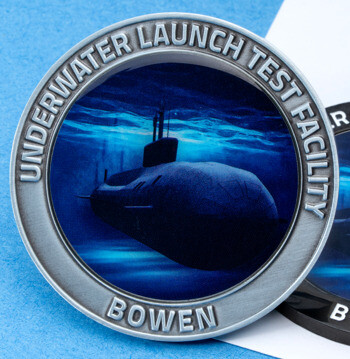 Two round challenge coins featuring a submarine underwater, labeled Underwater Launch Test Facility Bowen in silver and black metal finishes.