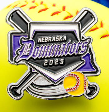 Softball lapel pin featuring Nebraska Dominators 2025 text, crossed bats, a home plate, and a yellow softball over a larger yellow softball background.