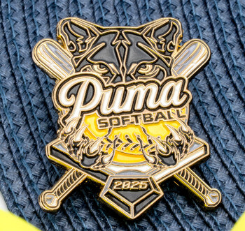 Custom enamel pin for Puma Softball 2025 featuring a cougar head, crossed bats, and a yellow softball over a blue textured background.
