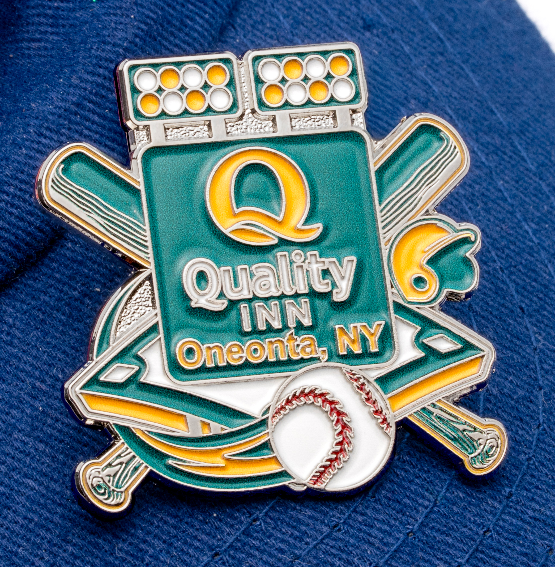 Enamel baseball lapel pin for Quality Inn Oneonta, NY featuring crossed bats, a baseball, stadium lights, and green and yellow accents on a blue hat.