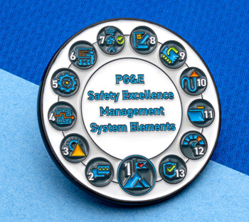 Circular custom enamel pin for PG&E Safety Excellence Management System Elements featuring thirteen numbered icons arranged in a ring on a white background.