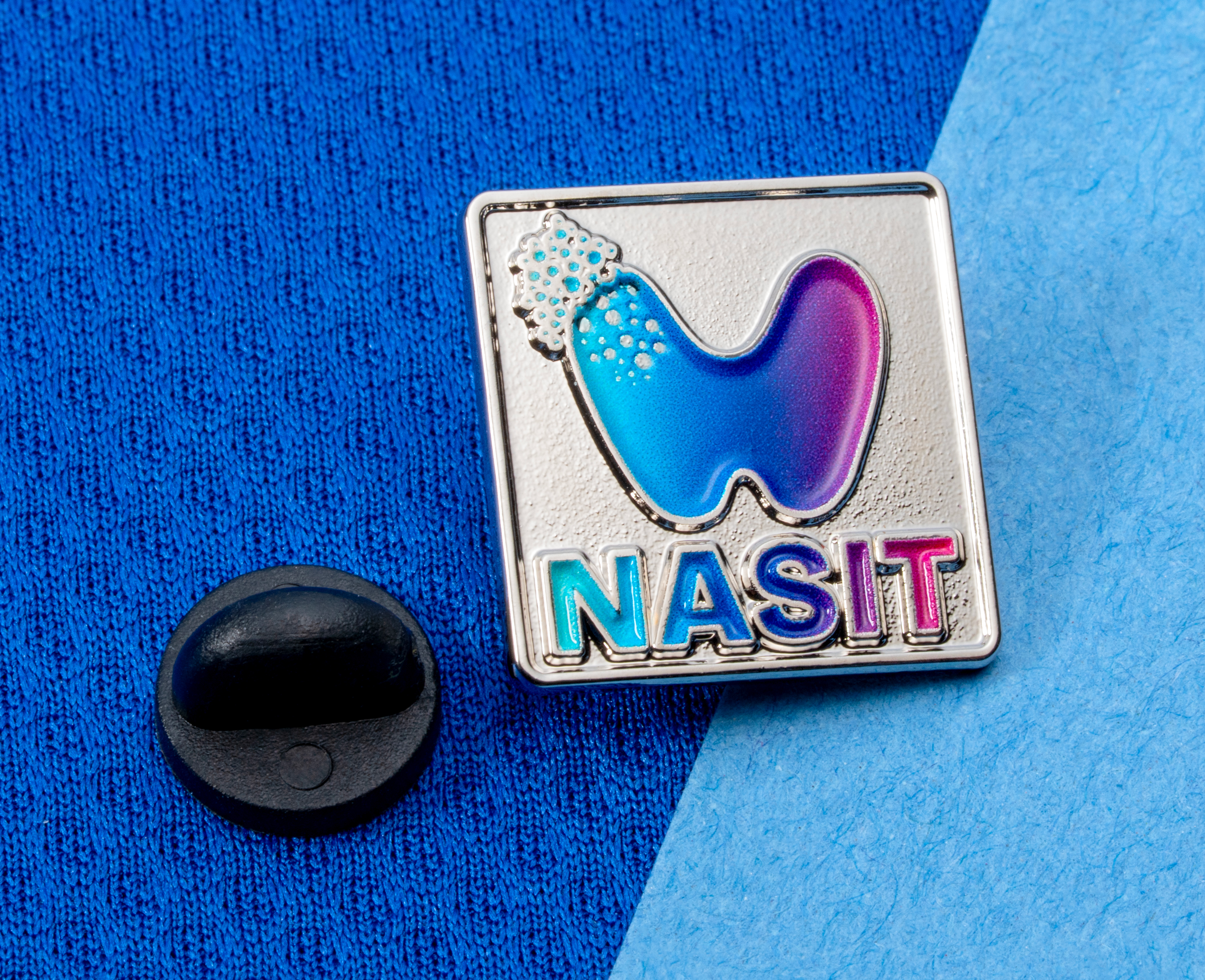 map[name:Square silver lapel pin with NASIT text and a blue to purple gradient logo on a blue textured background. naturalSort:Square silver lapel pin with NASIT text and a blue to purple gradient logo on a blue textured background.]