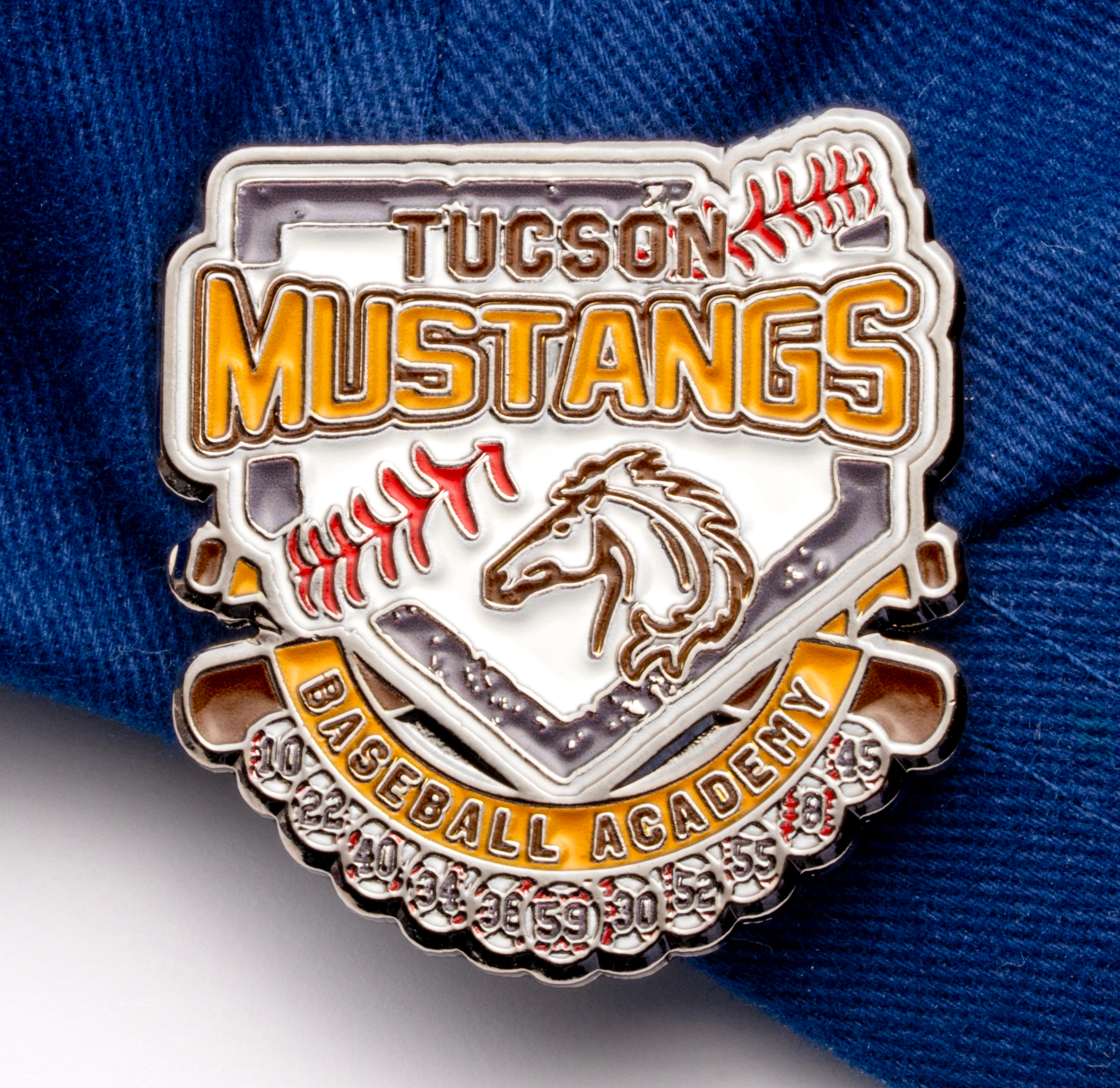 map[name:Enamel lapel pin for Tucson Mustangs Baseball Academy featuring a horse head logo, baseball diamond shape, and crossed bats on a blue fabric background. naturalSort:Enamel lapel pin for Tucson Mustangs Baseball Academy featuring a horse head logo, baseball diamond shape, and crossed bats on a blue fabric background.]