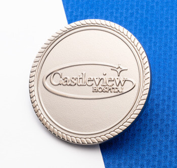 A circular silver coin featuring the Castleview Hospital logo with a rope border design, resting on a white and blue textured background.