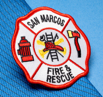 Embroidered Florian cross patch for San Marcos Fire & Rescue featuring a fire hydrant, axe, and ladder iconography on a blue textured background.