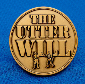 A circular brass challenge coin featuring the text The Utter Will and an illustration of a person and a skeleton sharing a drink.