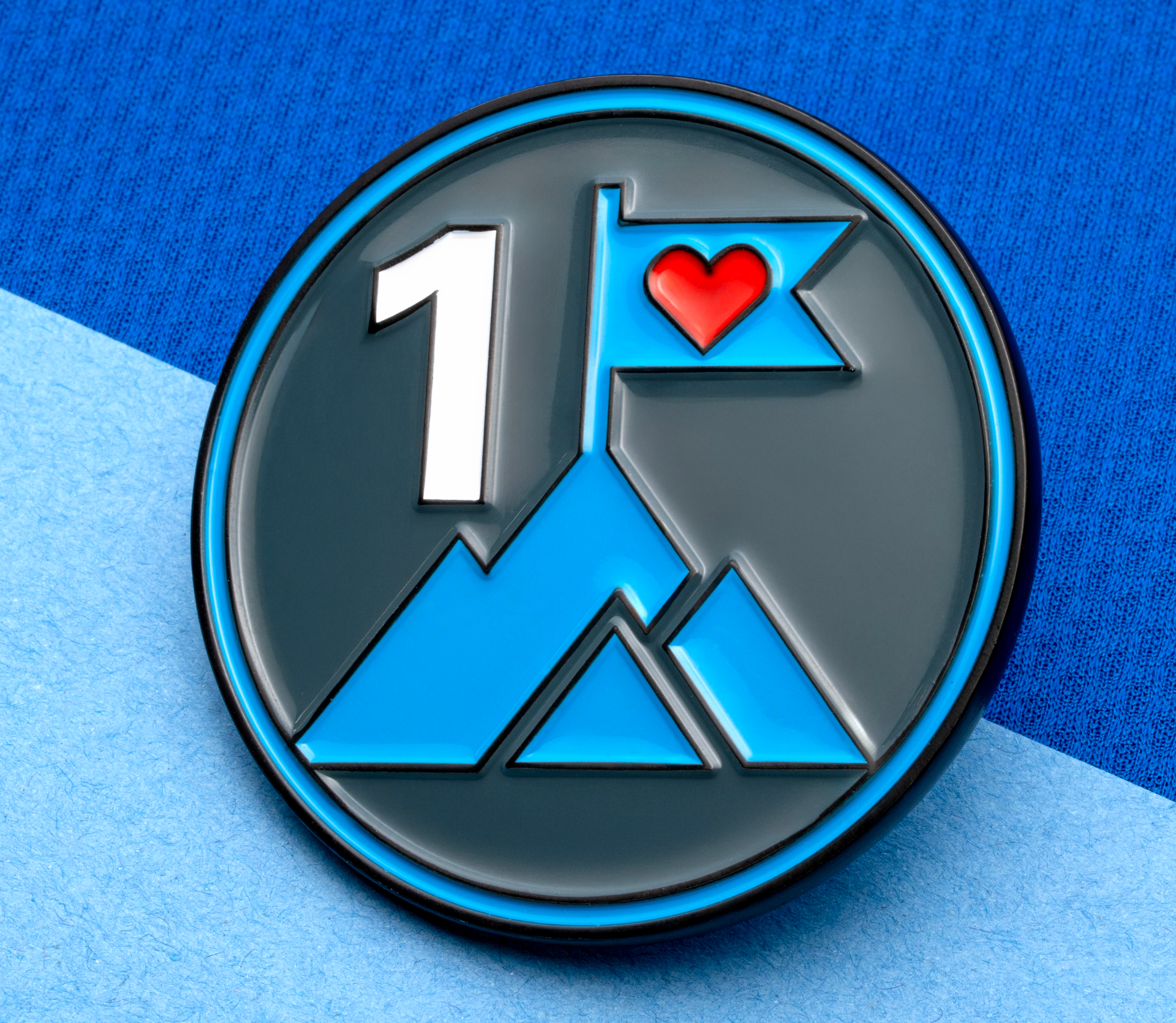 map[name:Circular enamel lapel pin featuring a number one, blue mountain peaks, and a flag with a red heart. naturalSort:Circular enamel lapel pin featuring a number one, blue mountain peaks, and a flag with a red heart.]