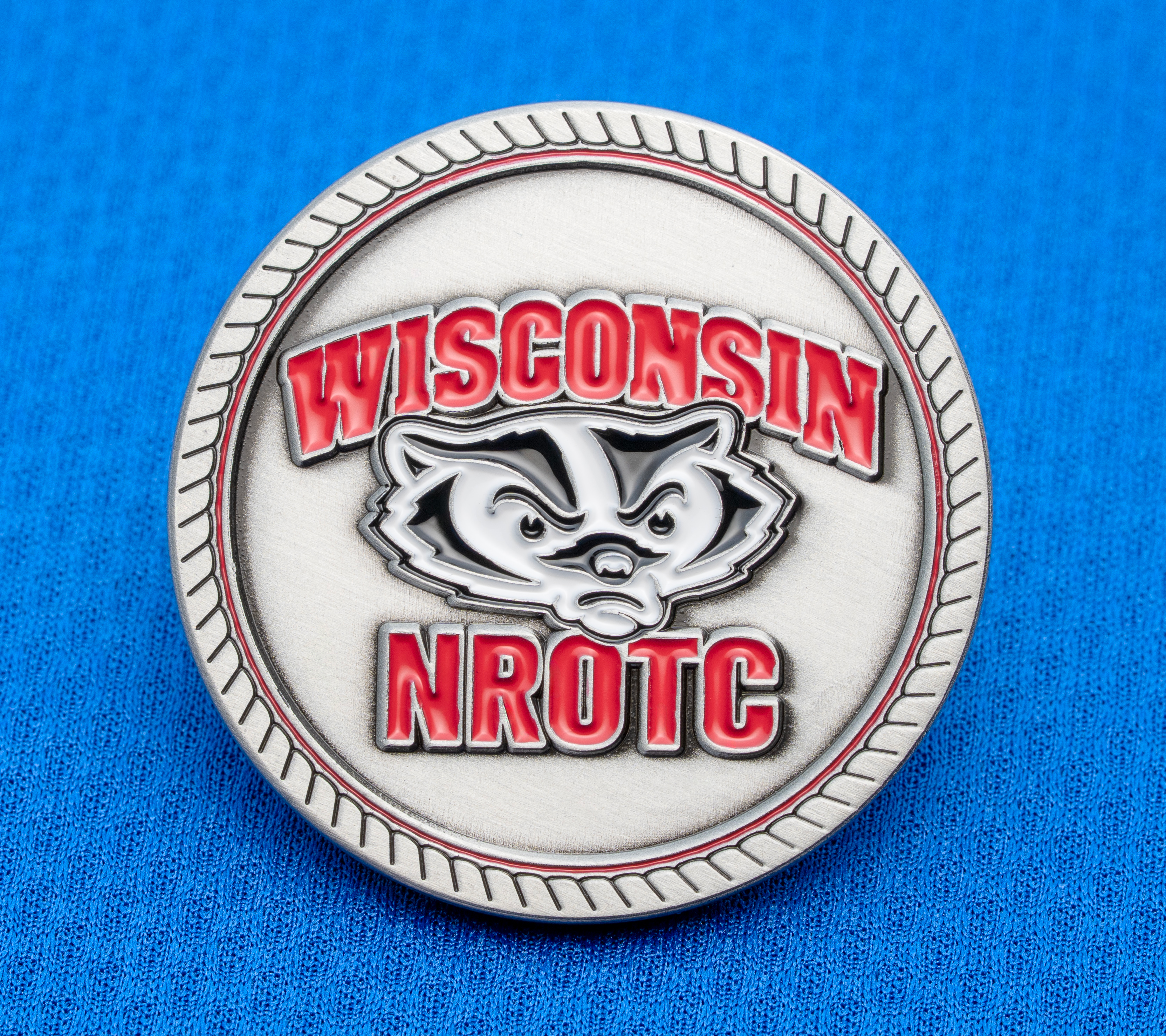 map[name:Circular silver medallion featuring the Wisconsin NROTC logo and Bucky Badger mascot in red and black enamel on a blue textured background. naturalSort:Circular silver medallion featuring the Wisconsin NROTC logo and Bucky Badger mascot in red and black enamel on a blue textured background.]
