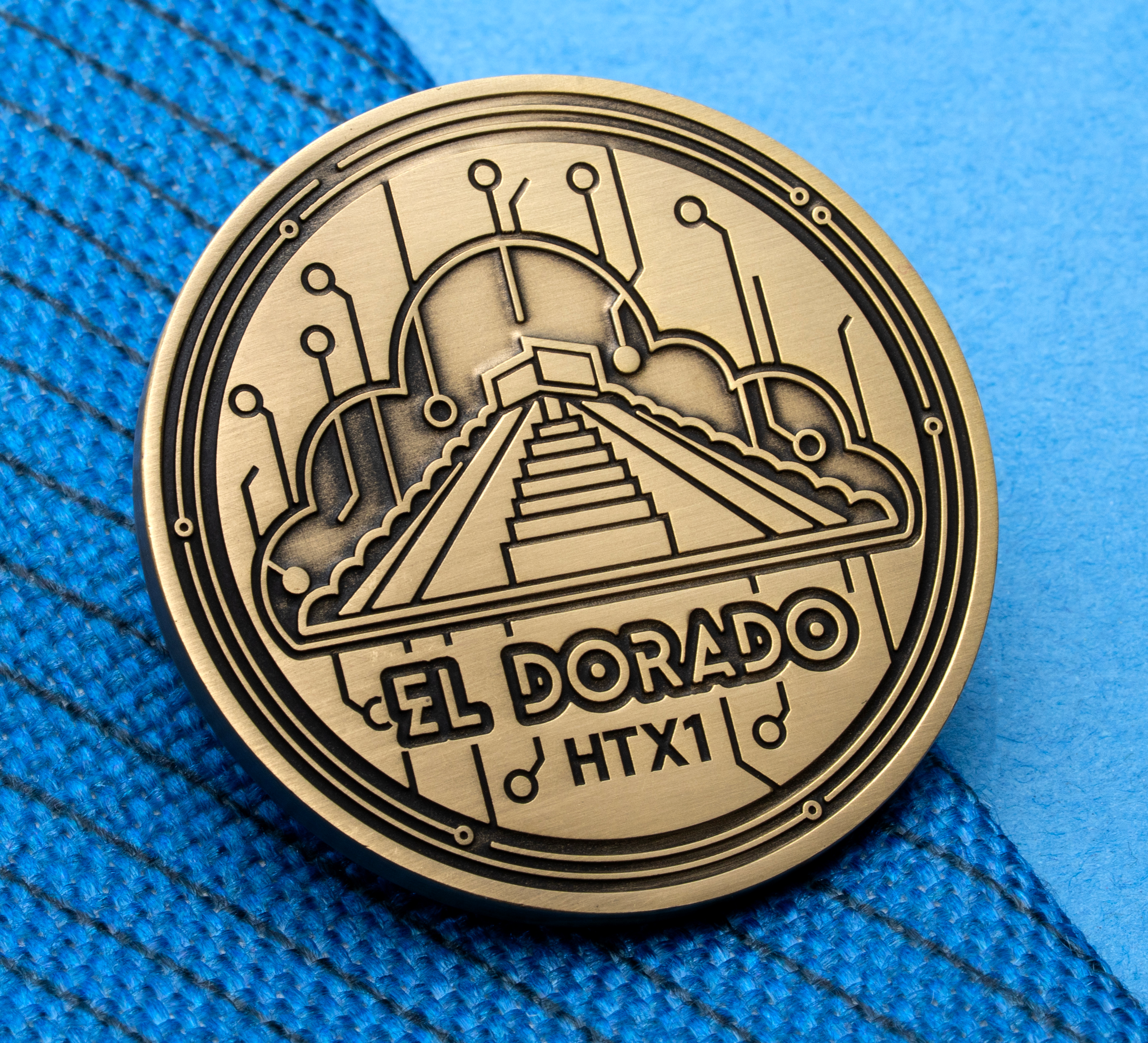 map[name:Antiqued gold circular lapel pin featuring El Dorado HTX1 text, a stepped pyramid, a cloud outline, and circuit board patterns on a blue textured background. naturalSort:Antiqued gold circular lapel pin featuring El Dorado HTX00000000000000000000000000000001.00000000000000000000000000000000  text, a stepped pyramid, a cloud outline, and circuit board patterns on a blue textured background.]