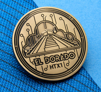 Antiqued gold circular lapel pin featuring El Dorado HTX1 text, a stepped pyramid, a cloud outline, and circuit board patterns on a blue textured background.