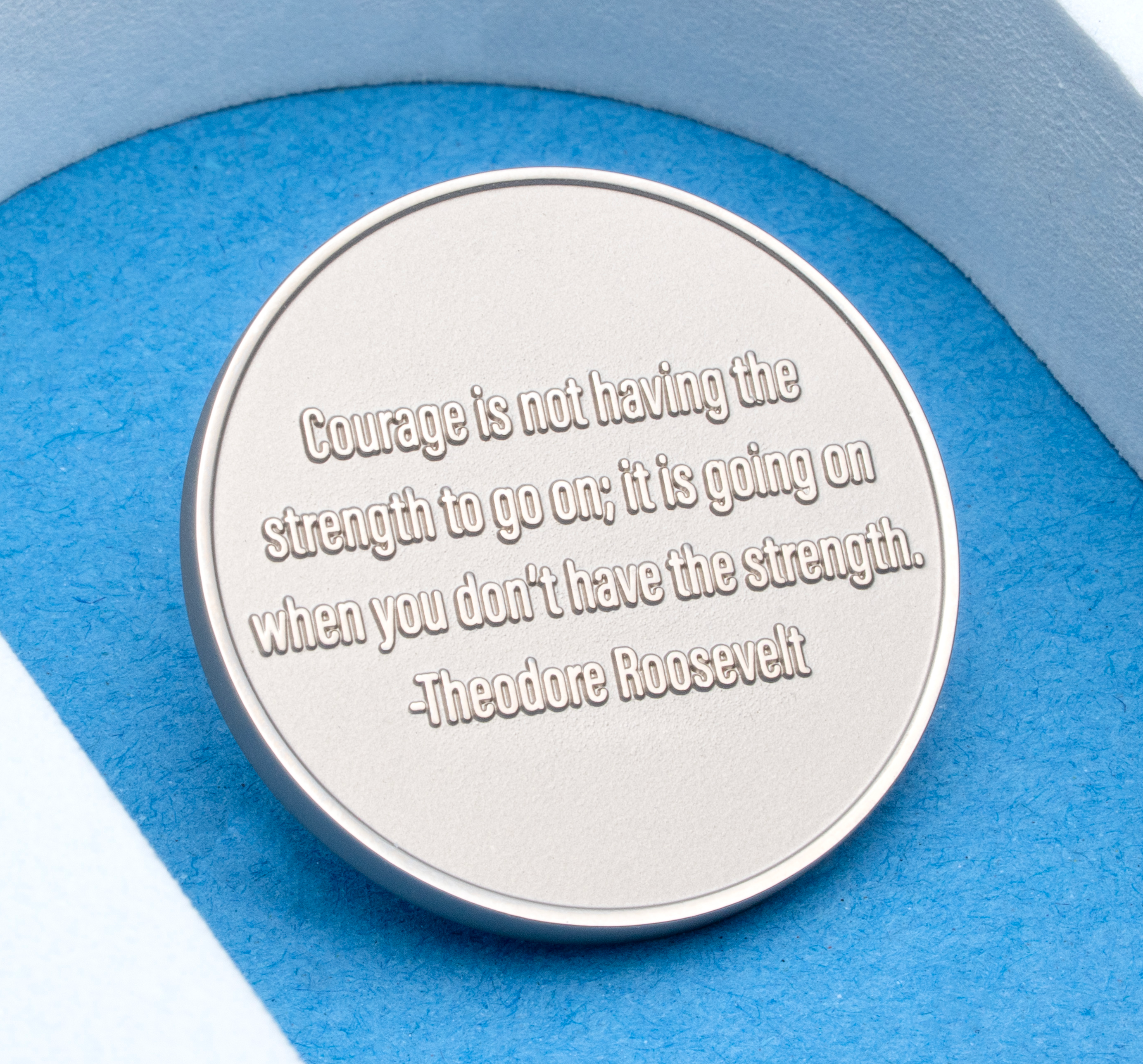 map[name:Silver round medallion engraved with a Theodore Roosevelt quote on courage, displayed under a white arch on a blue background. naturalSort:Silver round medallion engraved with a Theodore Roosevelt quote on courage, displayed under a white arch on a blue background.]