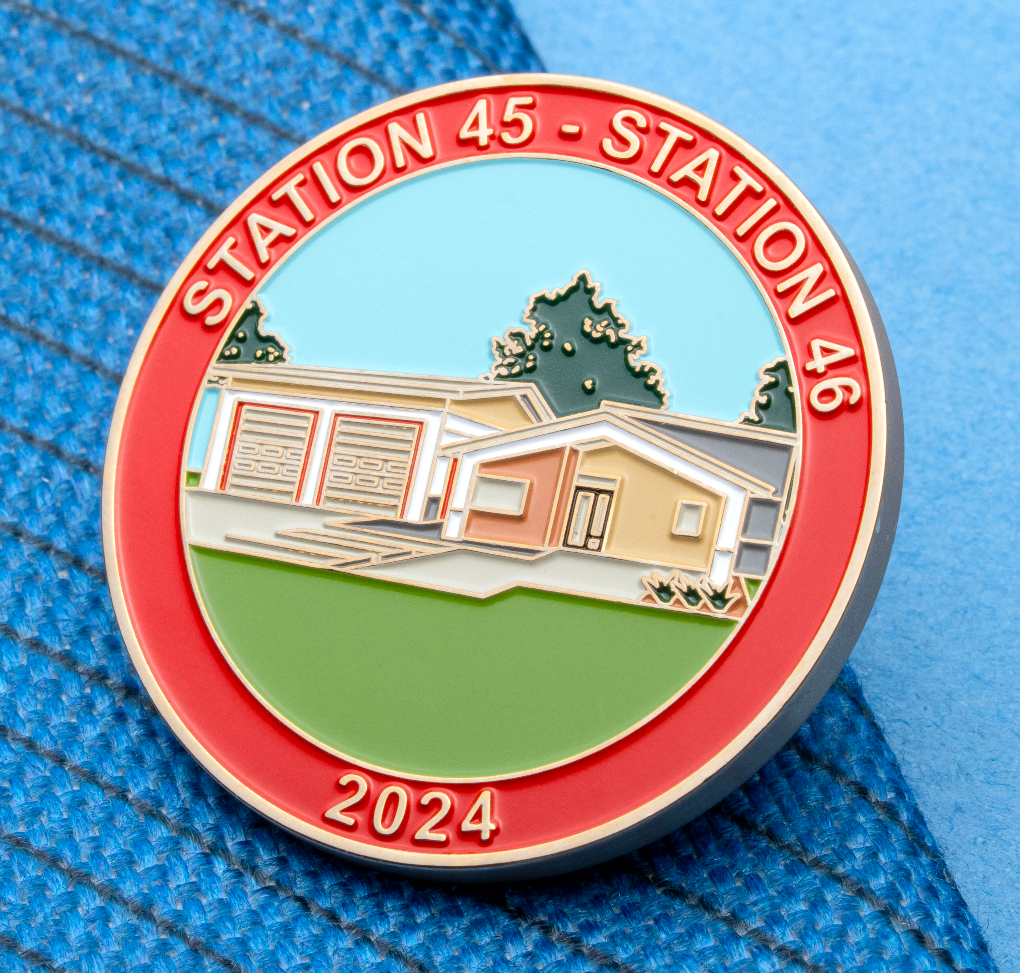 Circular enamel lapel pin for Station 45 and Station 46 featuring a fire station building illustration, green lawn, and the year 2024 on a red border.