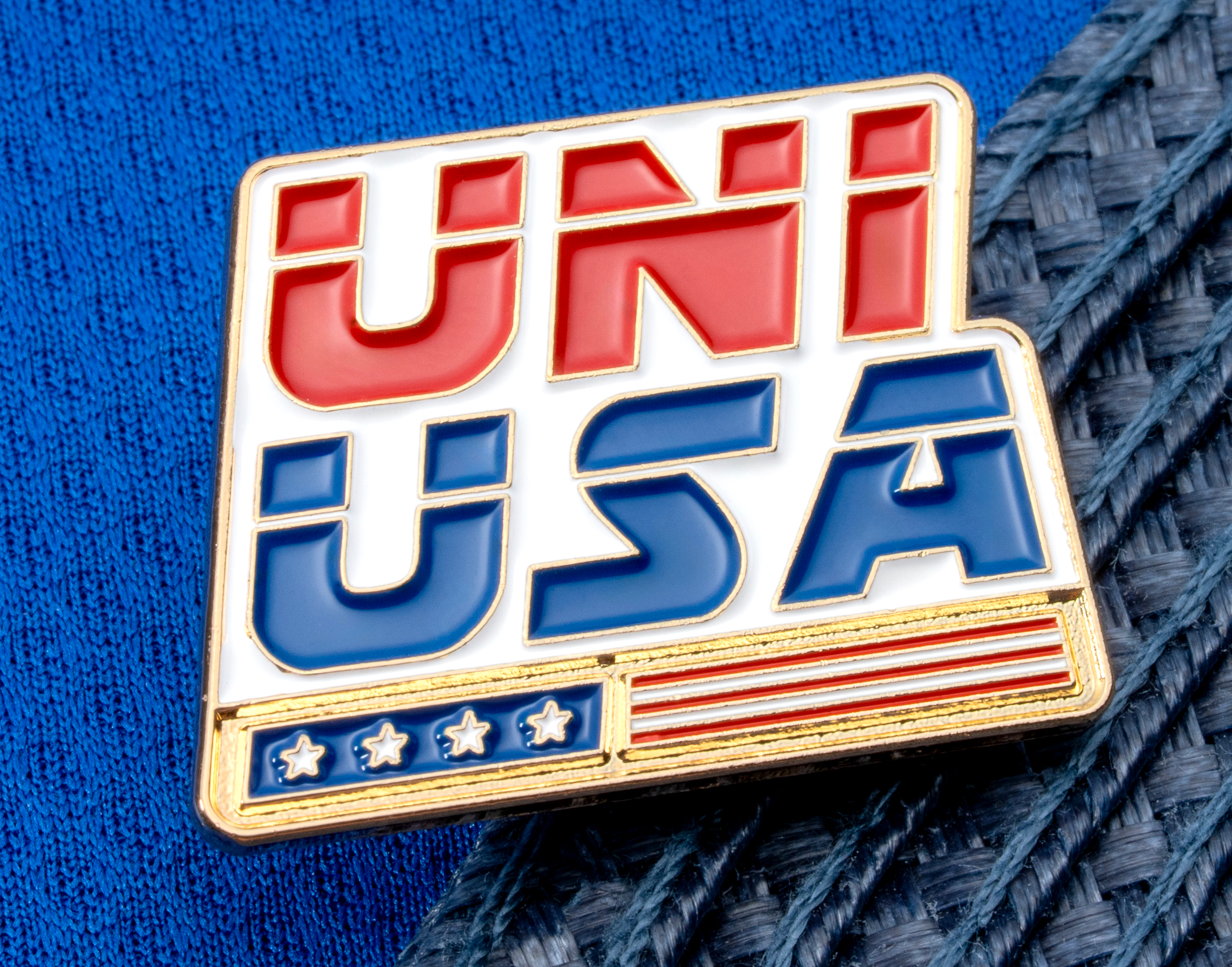 map[name:Enamel lapel pin with 'UNI USA' text in red and blue letters above a stylized American flag design on a blue textured background. naturalSort:Enamel lapel pin with 'UNI USA' text in red and blue letters above a stylized American flag design on a blue textured background.]
