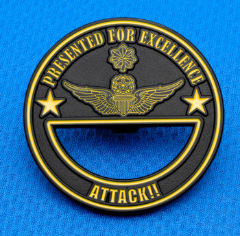 Circular black and gold medallion featuring a winged emblem and the text Presented For Excellence Attack on a blue fabric background.