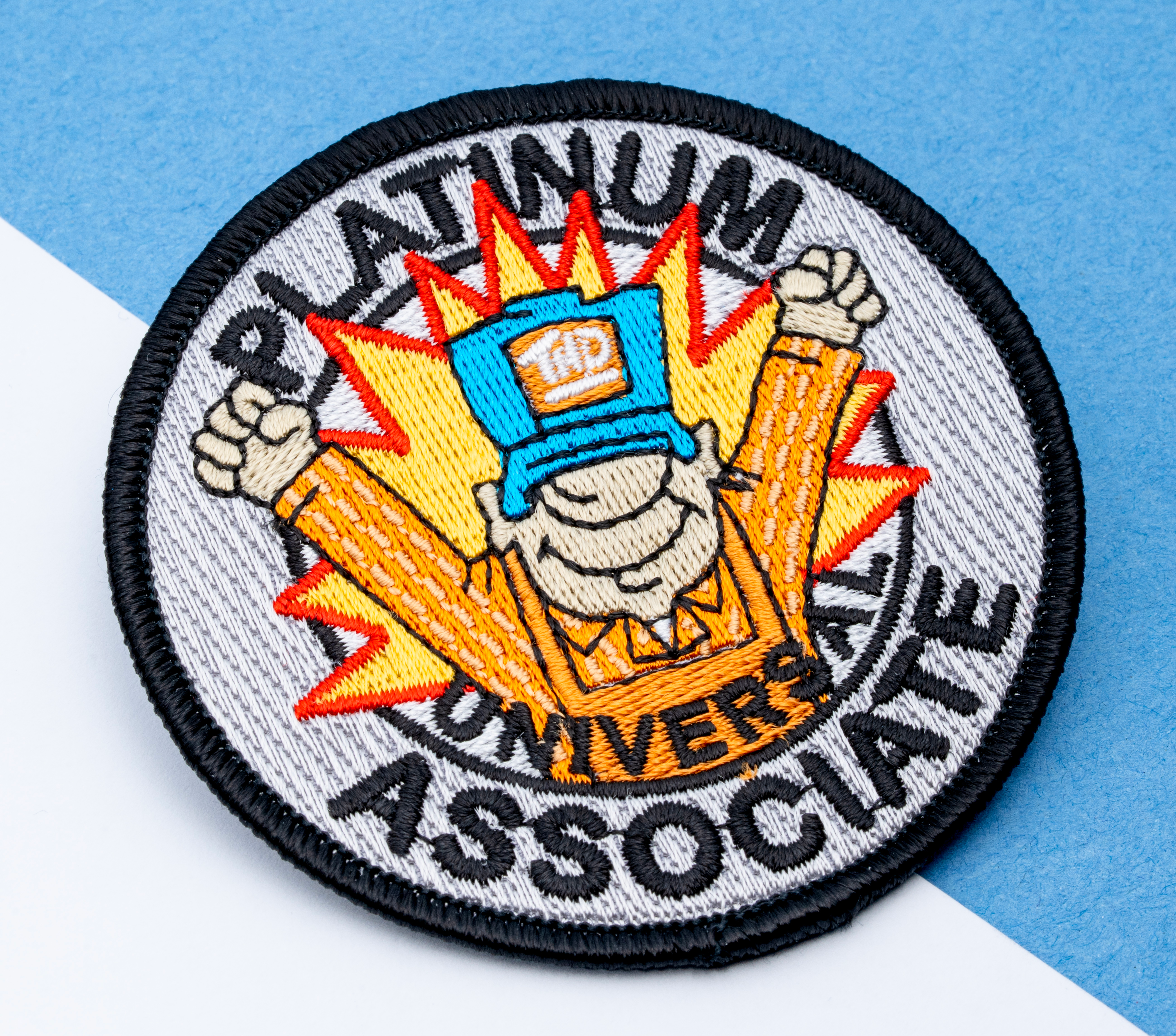 map[name:Circular embroidered patch with a cartoon character in an orange shirt and blue hat, surrounded by an orange sunburst and the text Platinum Universal Associate. naturalSort:Circular embroidered patch with a cartoon character in an orange shirt and blue hat, surrounded by an orange sunburst and the text Platinum Universal Associate.]