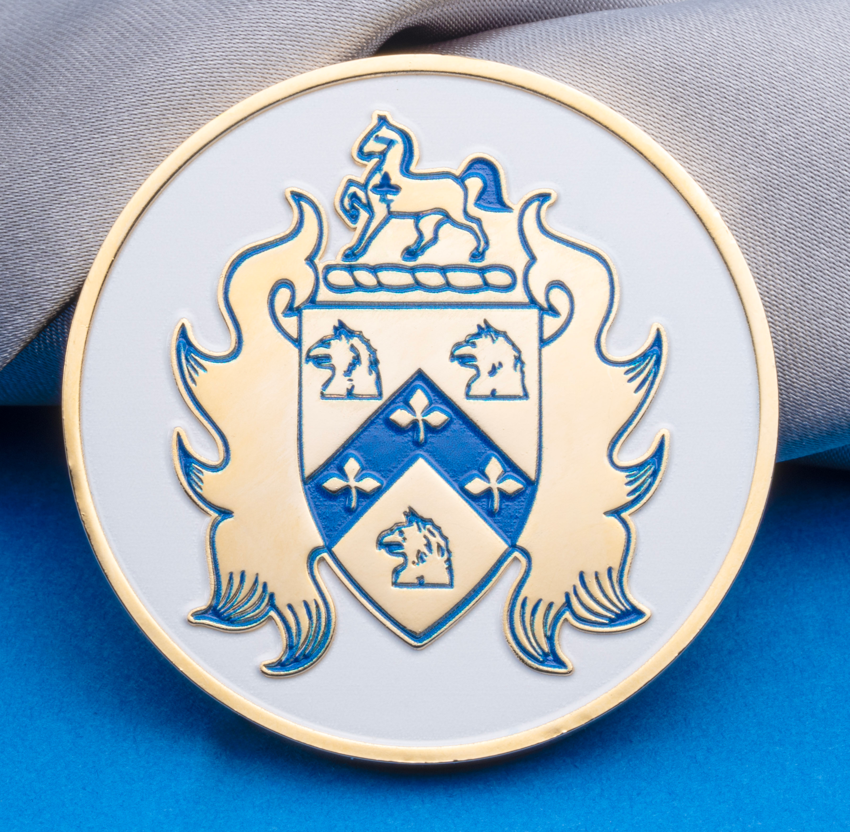 Circular challenge coin featuring a gold and blue heraldic shield and horse crest on a white enamel background.