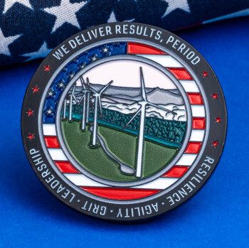Circular challenge coin featuring a wind farm landscape and American flag border, resting on a flag backdrop.