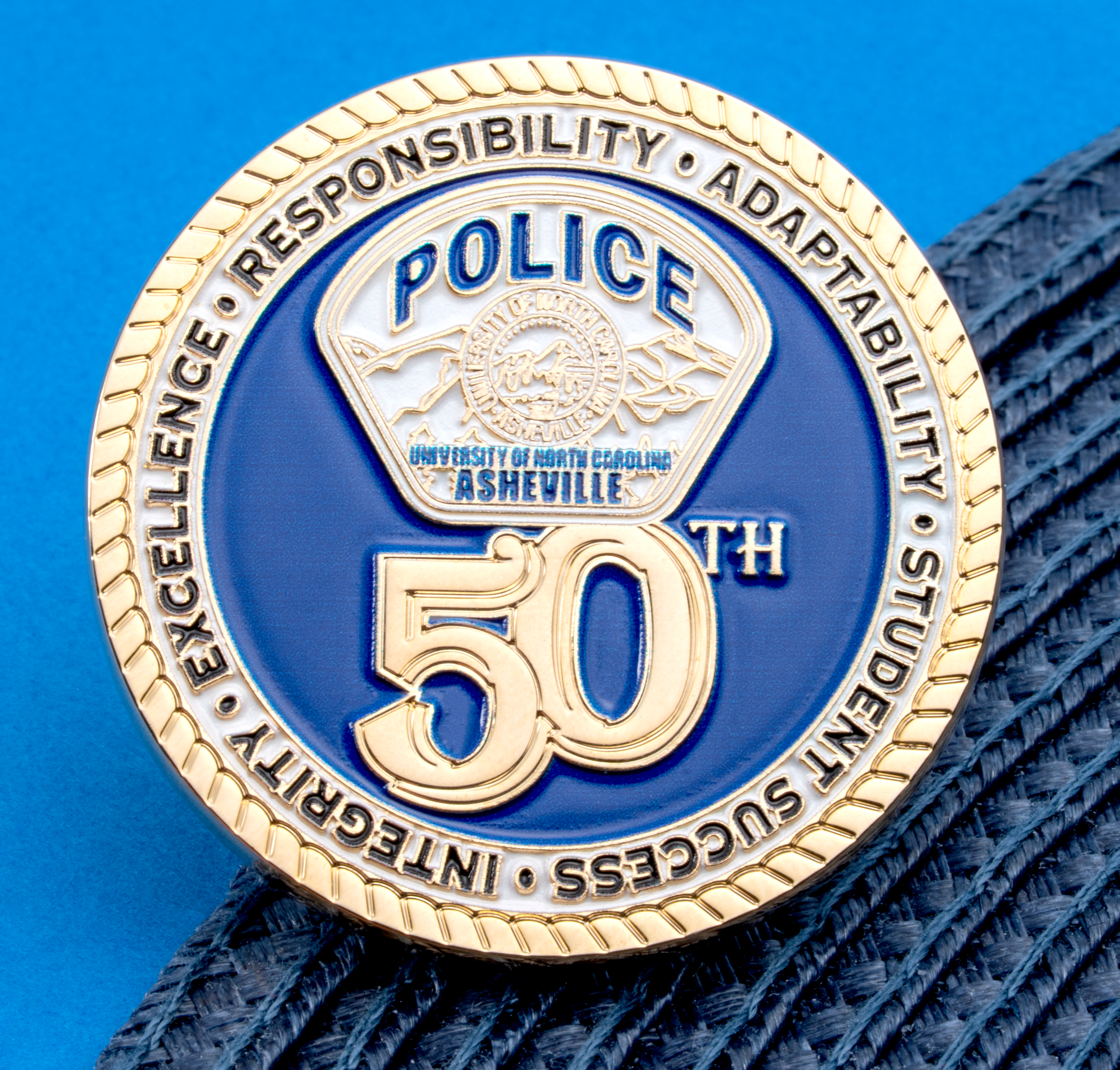 Blue and gold UNC Asheville Police 50th anniversary challenge coin with a rope border and core values text.