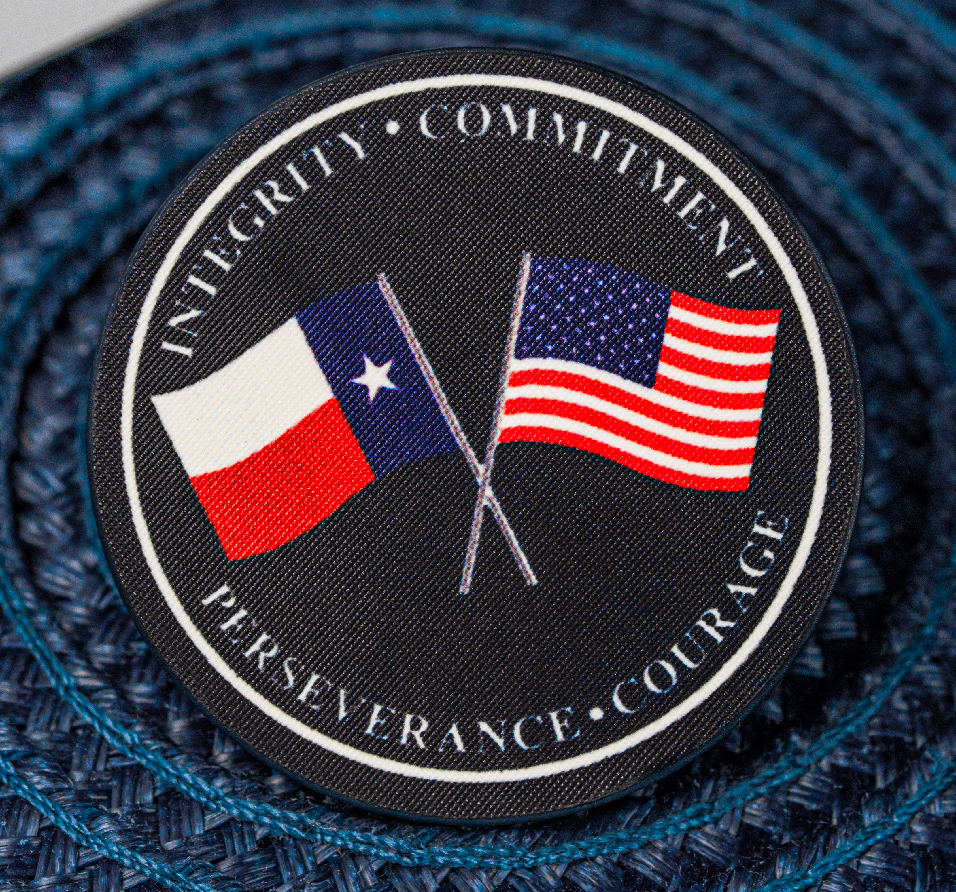 Circular embroidered patch featuring crossed Texas and United States flags with the words Integrity, Commitment, Perseverance, and Courage.