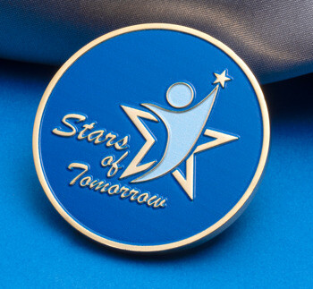 Circular blue challenge coin featuring the Stars of Tomorrow logo with a stylized figure and star on a gold-rimmed background.