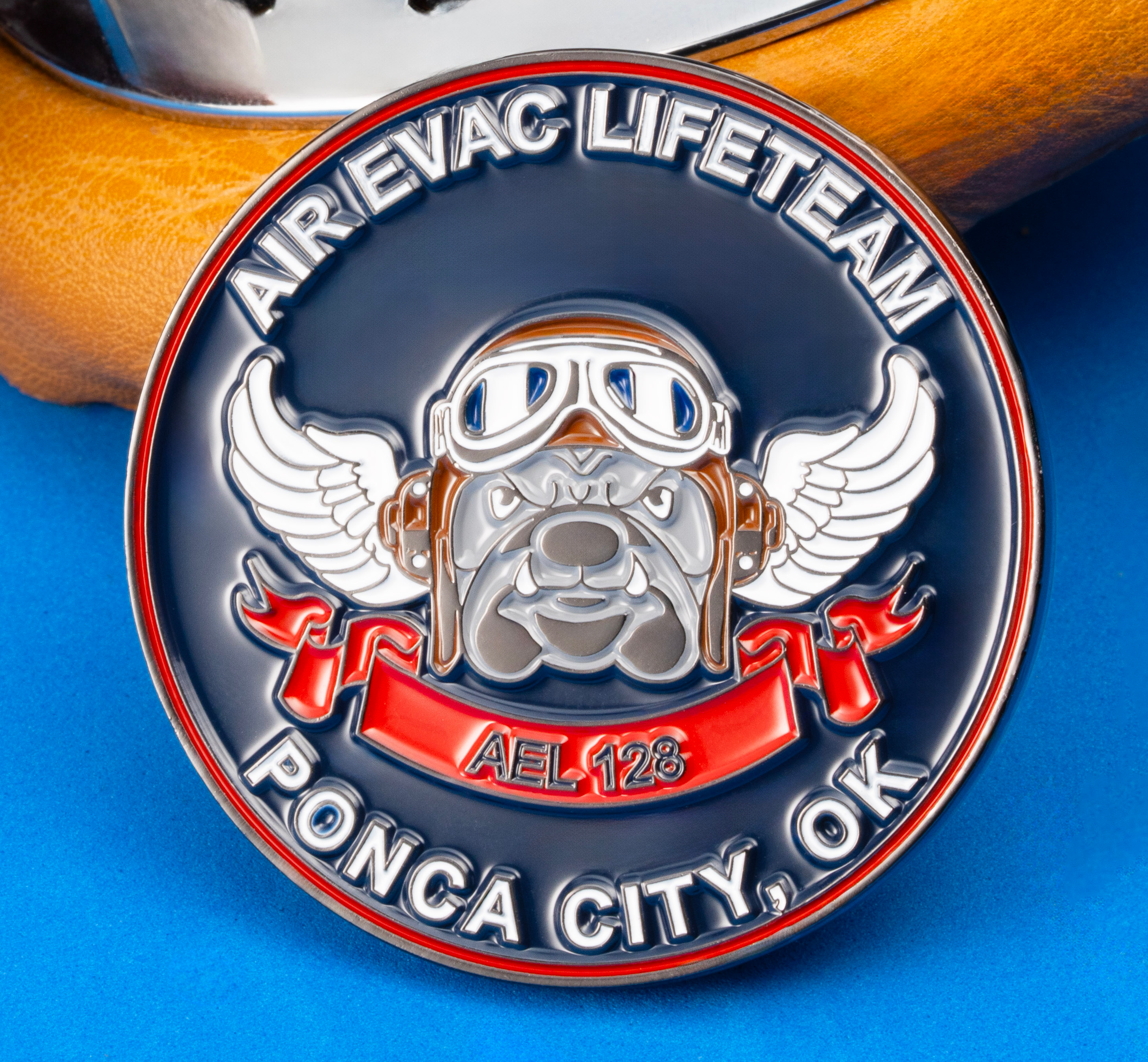 Air Evac Lifeteam Ponca City challenge coin featuring a winged bulldog wearing flight goggles, positioned next to leather aviation goggles.