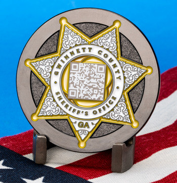 Gwinnett County Sheriff's Office challenge coin with a gold star, QR code, and GA label, displayed over an American flag background.