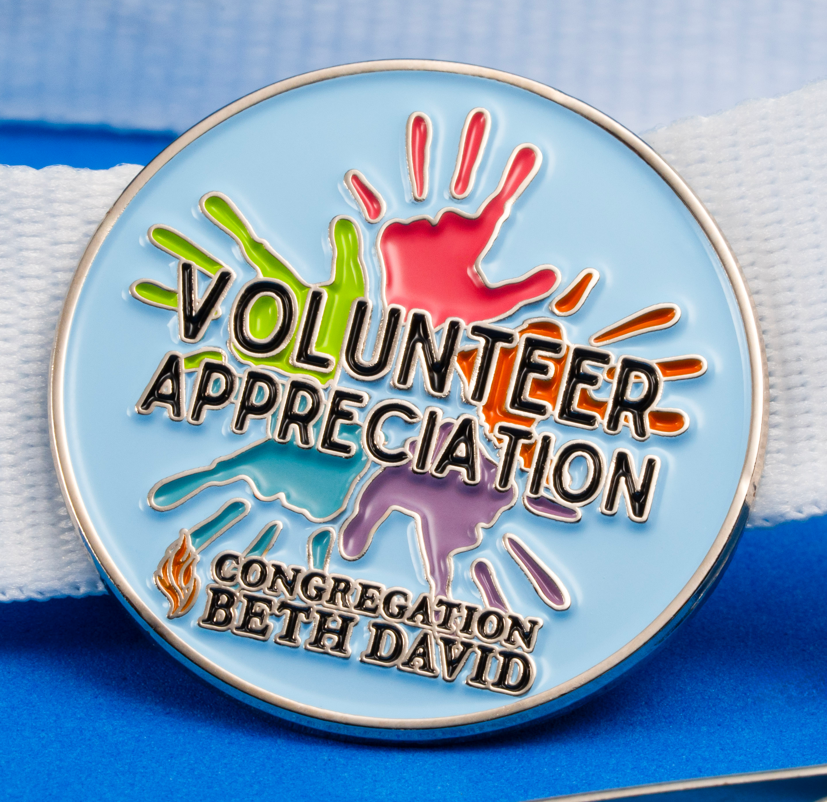 Enamel medal featuring colorful handprints and Volunteer Appreciation text for Congregation Beth David attached to a white lanyard.