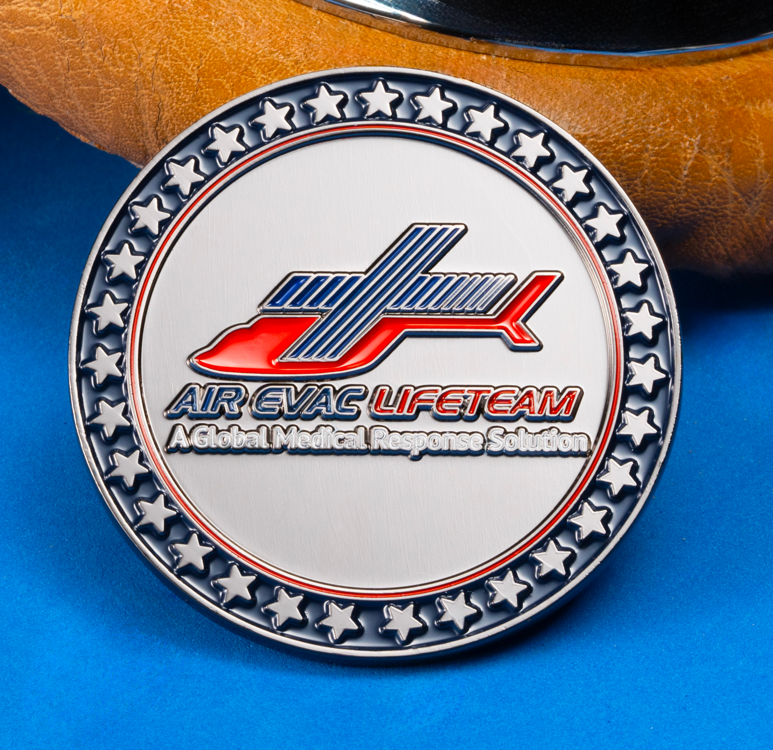 Air Evac Lifeteam challenge coin with red helicopter logo and star-patterned border resting against flight goggles.