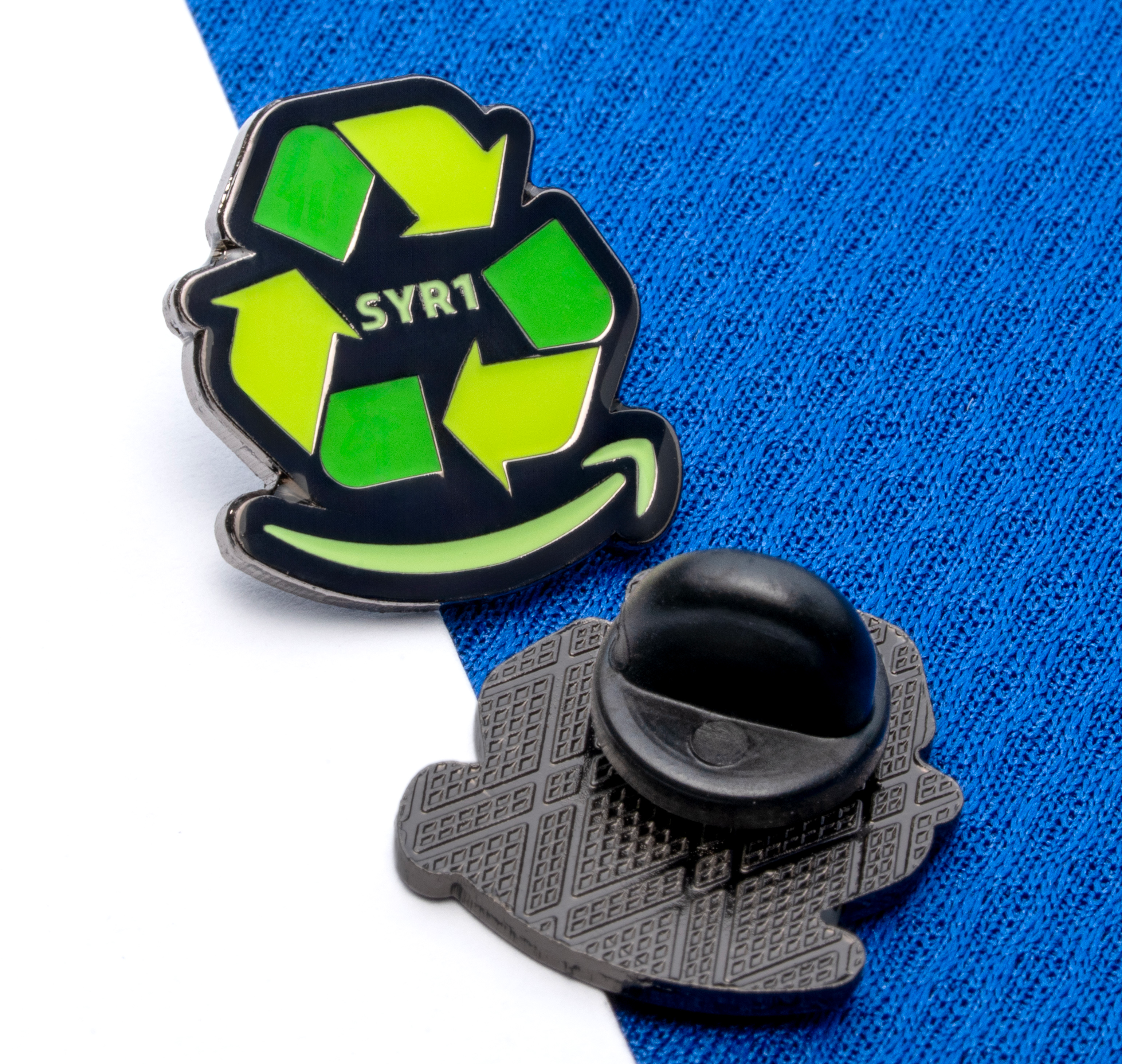 Enamel lapel pin featuring a green recycle symbol with the text SYR1 and a yellow smile logo on a black background.