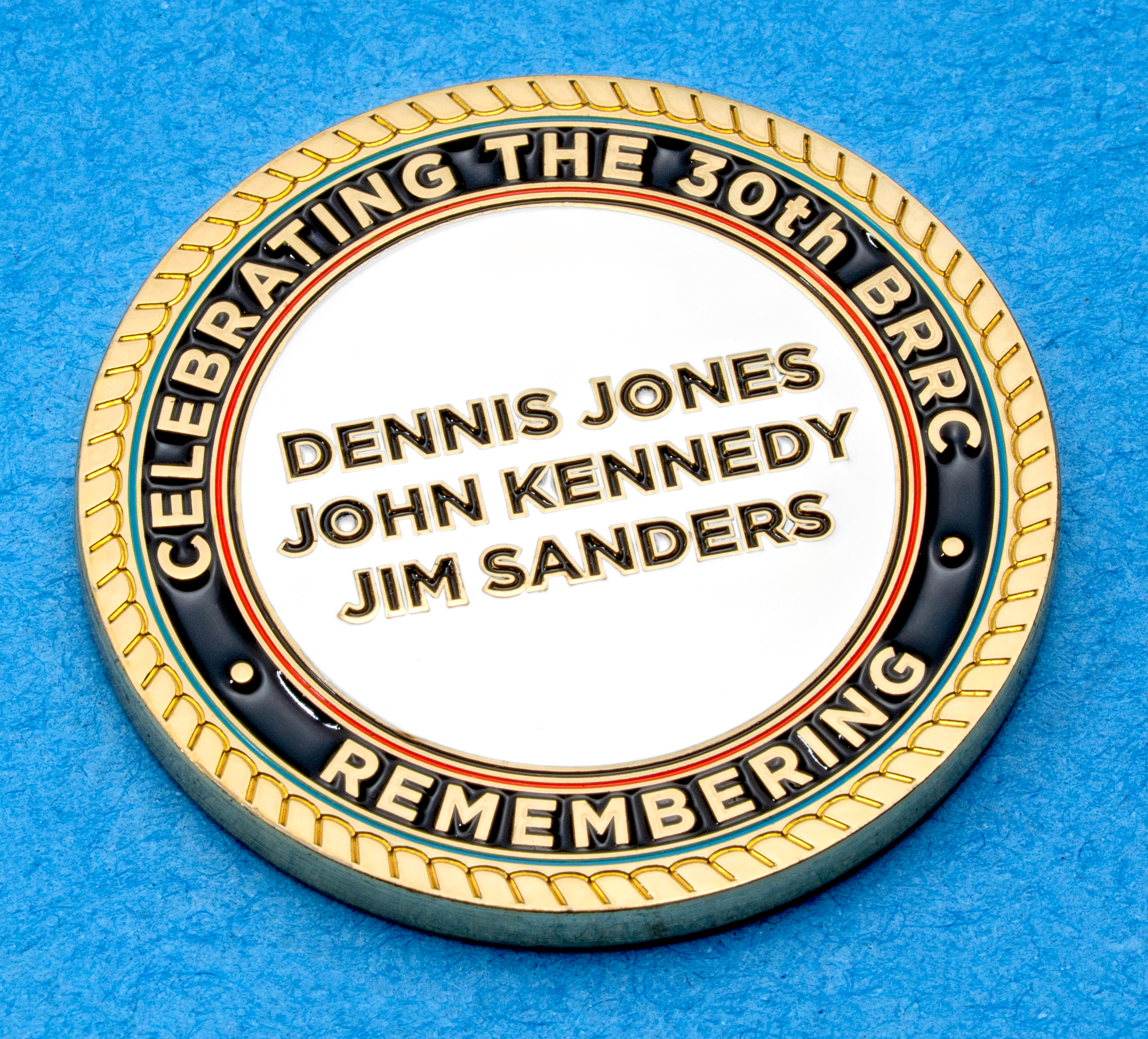 Gold challenge coin with rope border featuring the names Dennis Jones, John Kennedy, and Jim Sanders for the 30th BRRC anniversary.