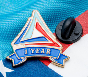 Triangular lapel pin with 1 year service banner on an American flag and blue fabric background.