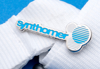 Synthomer brand lapel pin with blue enamel lettering and a silver circular logo on a white lanyard.
