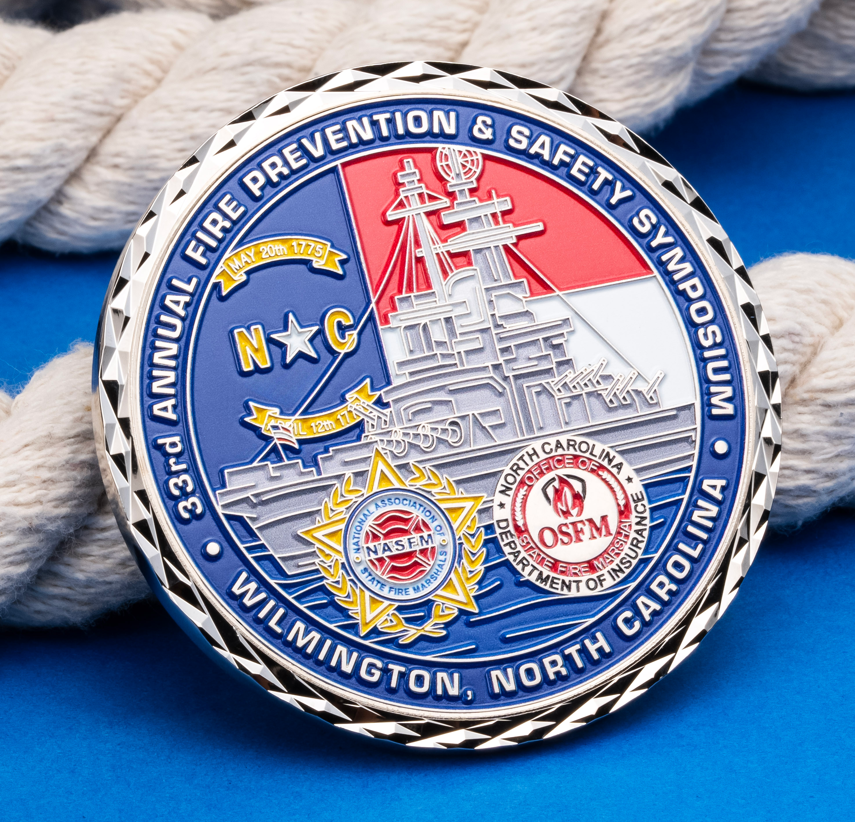 33rd Annual Fire Prevention & Safety Symposium challenge coin with battleship illustration and OSFM seal on a blue background with rope.