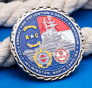 33rd Annual Fire Prevention & Safety Symposium challenge coin with battleship illustration and OSFM seal on a blue background with rope.