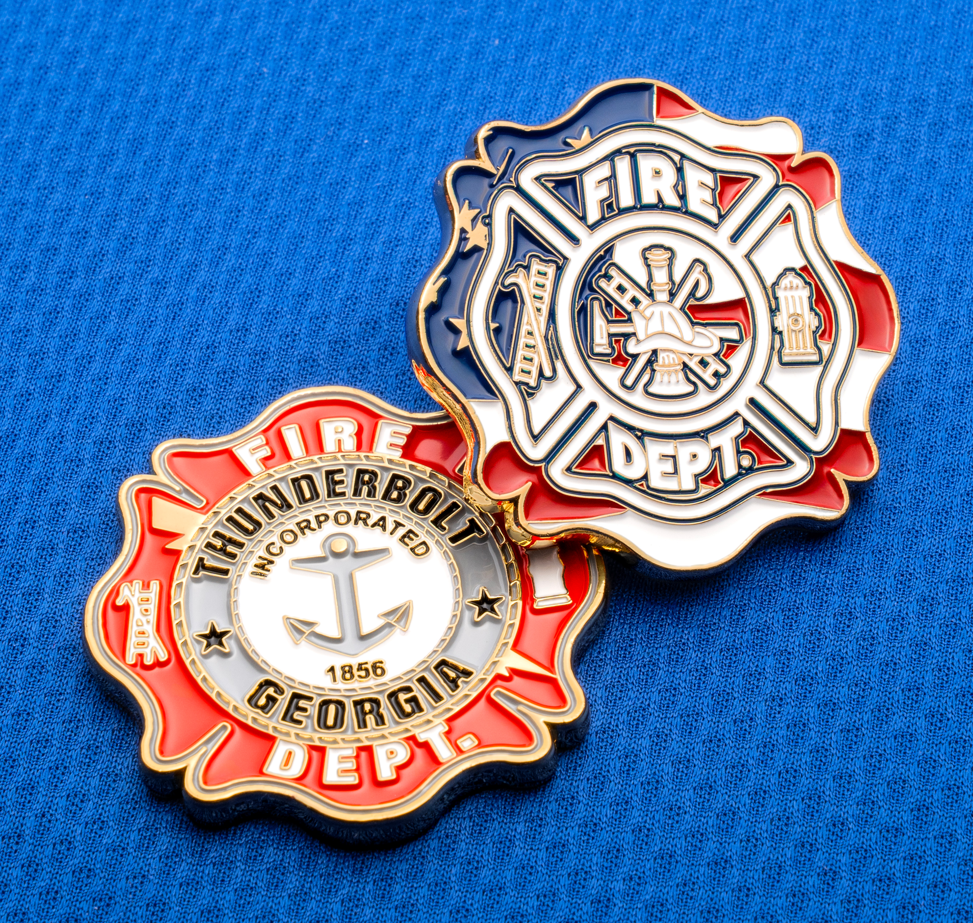 Two Maltese cross lapel pins on blue fabric featuring Thunderbolt Georgia Fire Dept and American flag designs.