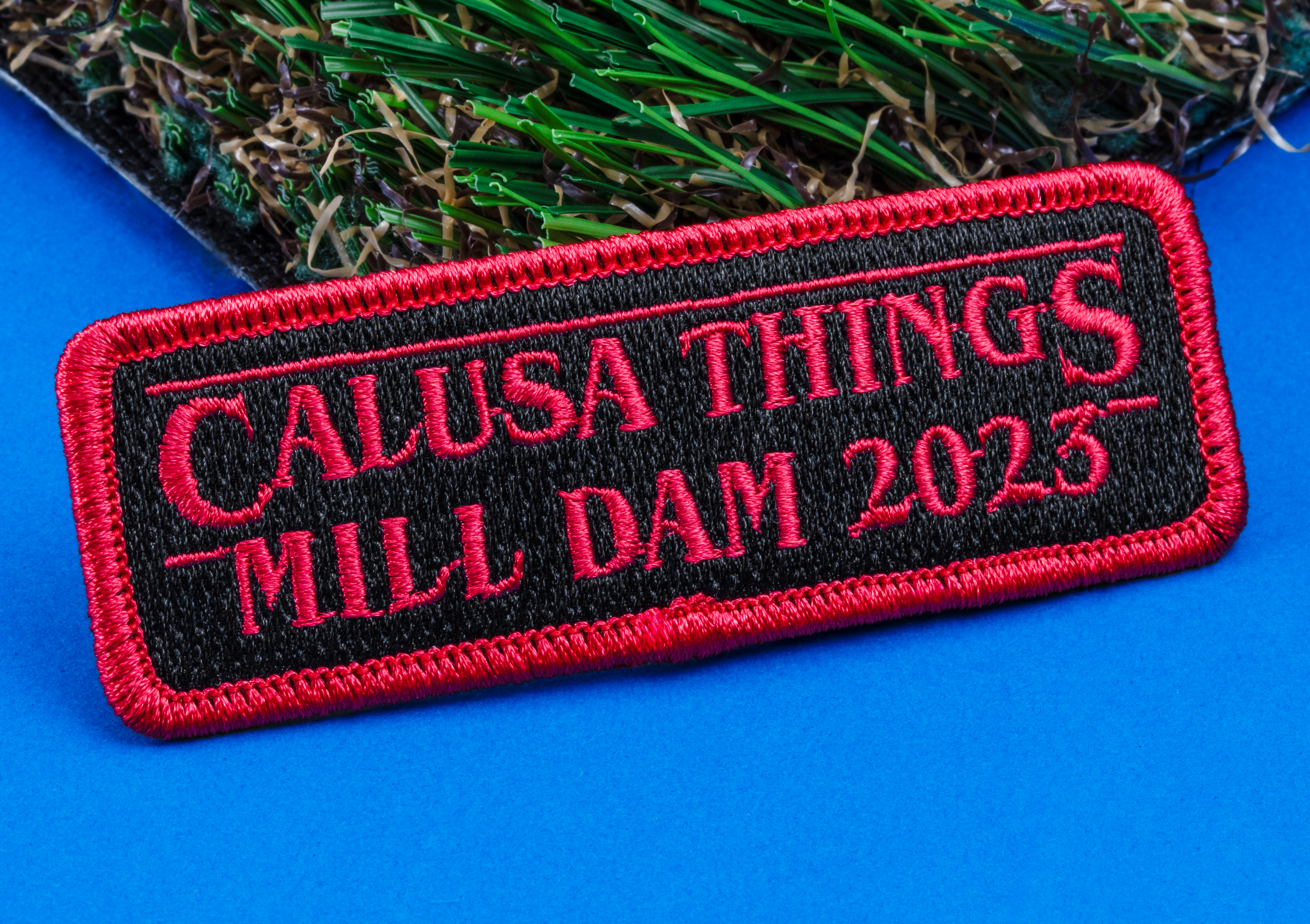 Rectangular embroidered patch with red text reading Calusa Things Mill Dam 2023 on a black background with a red border.