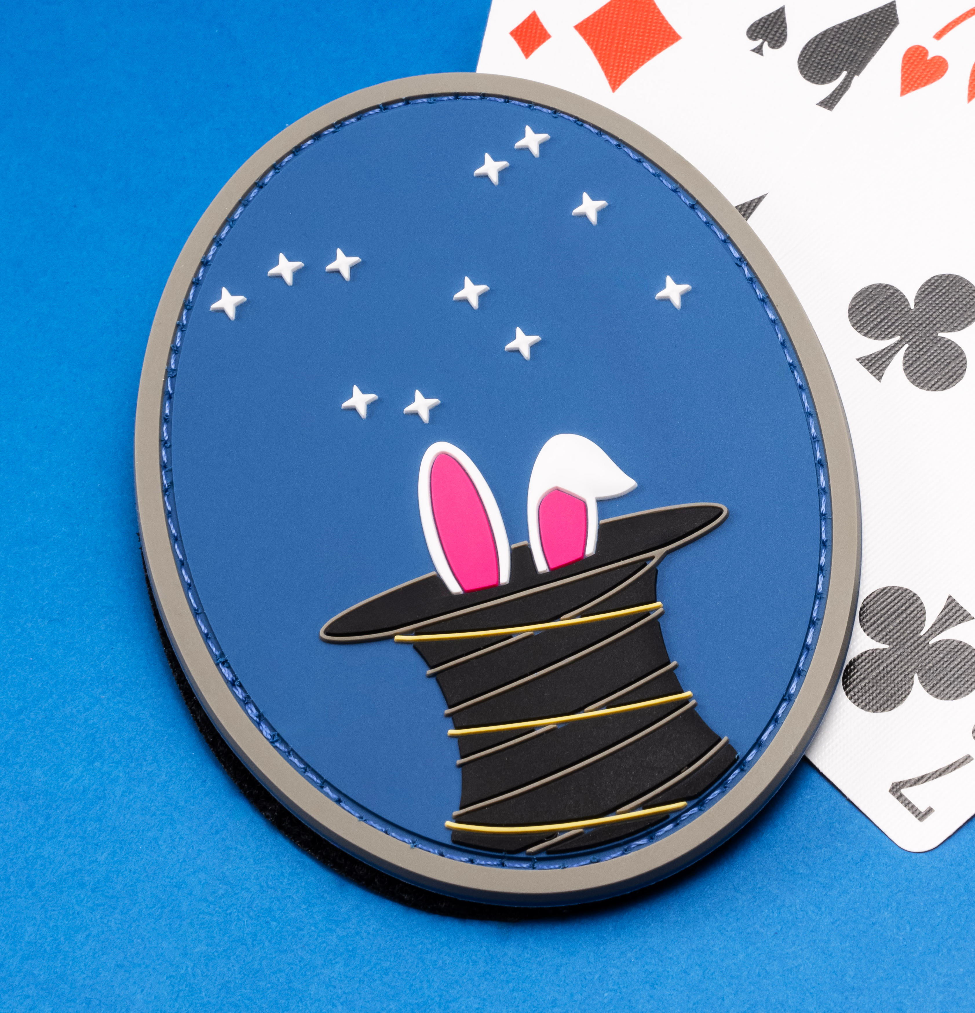 Oval PVC patch featuring a magician's top hat with rabbit ears and stars, displayed next to playing cards.