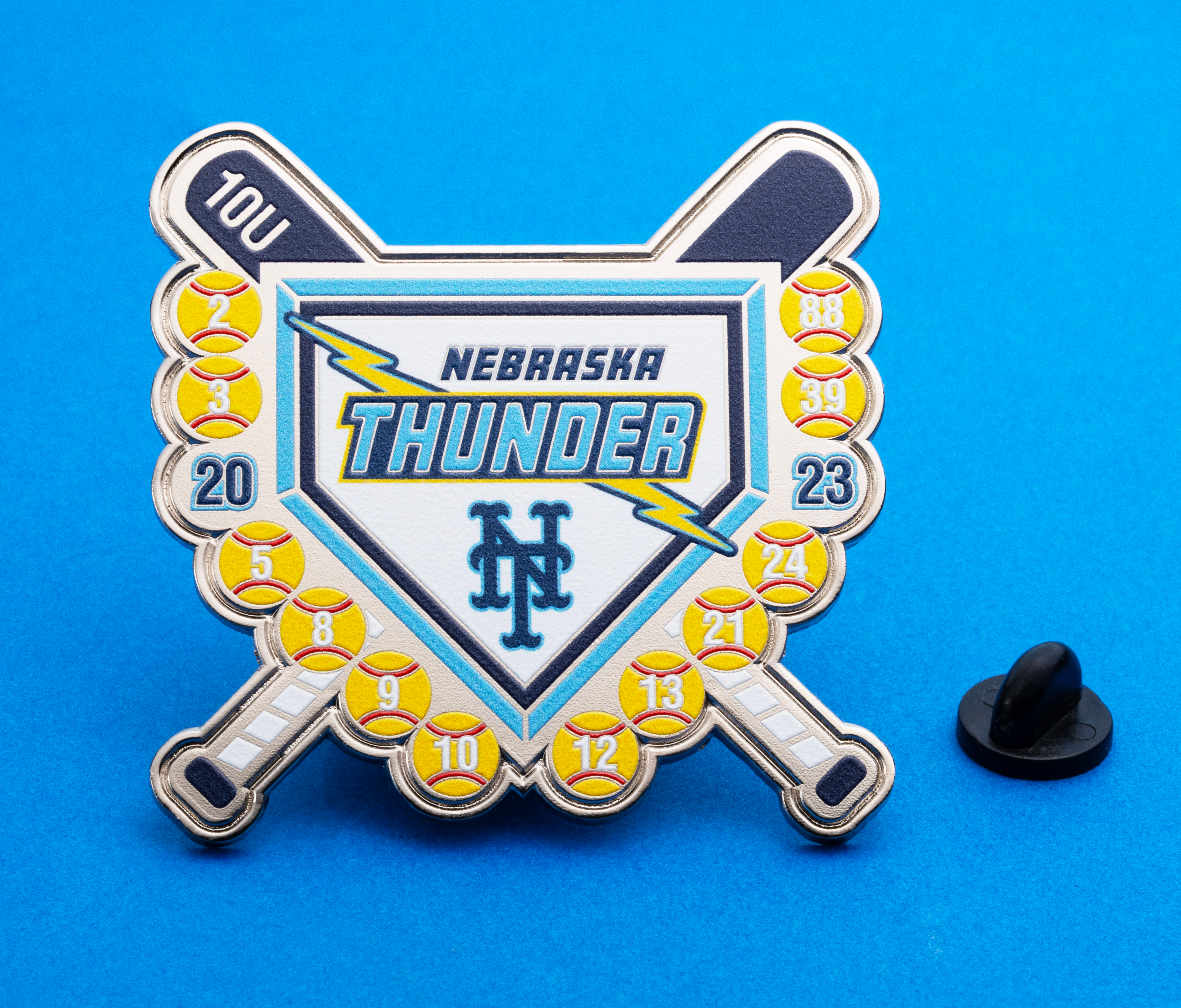 Shield shaped softball trading pin featuring Nebraska Thunder text, crossed bats, lightning bolt, and numbered softballs.