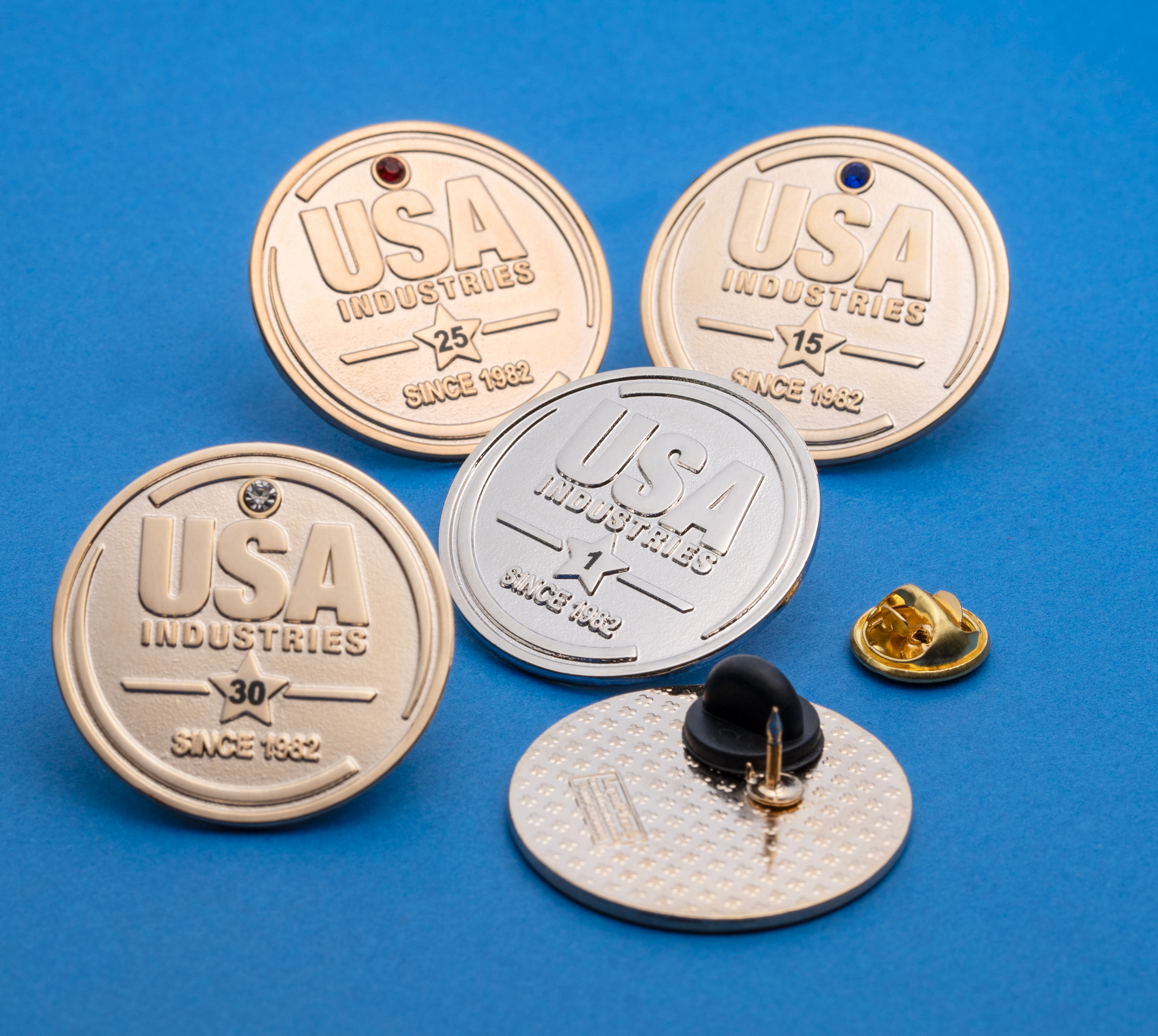Set of gold and silver USA Industries anniversary lapel pins with various colored gemstones and years of service.