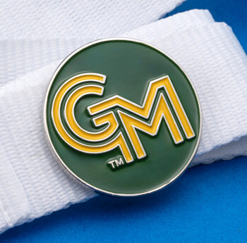 A circular green and yellow GM logo lapel pin attached to a white fabric lanyard over a blue surface.