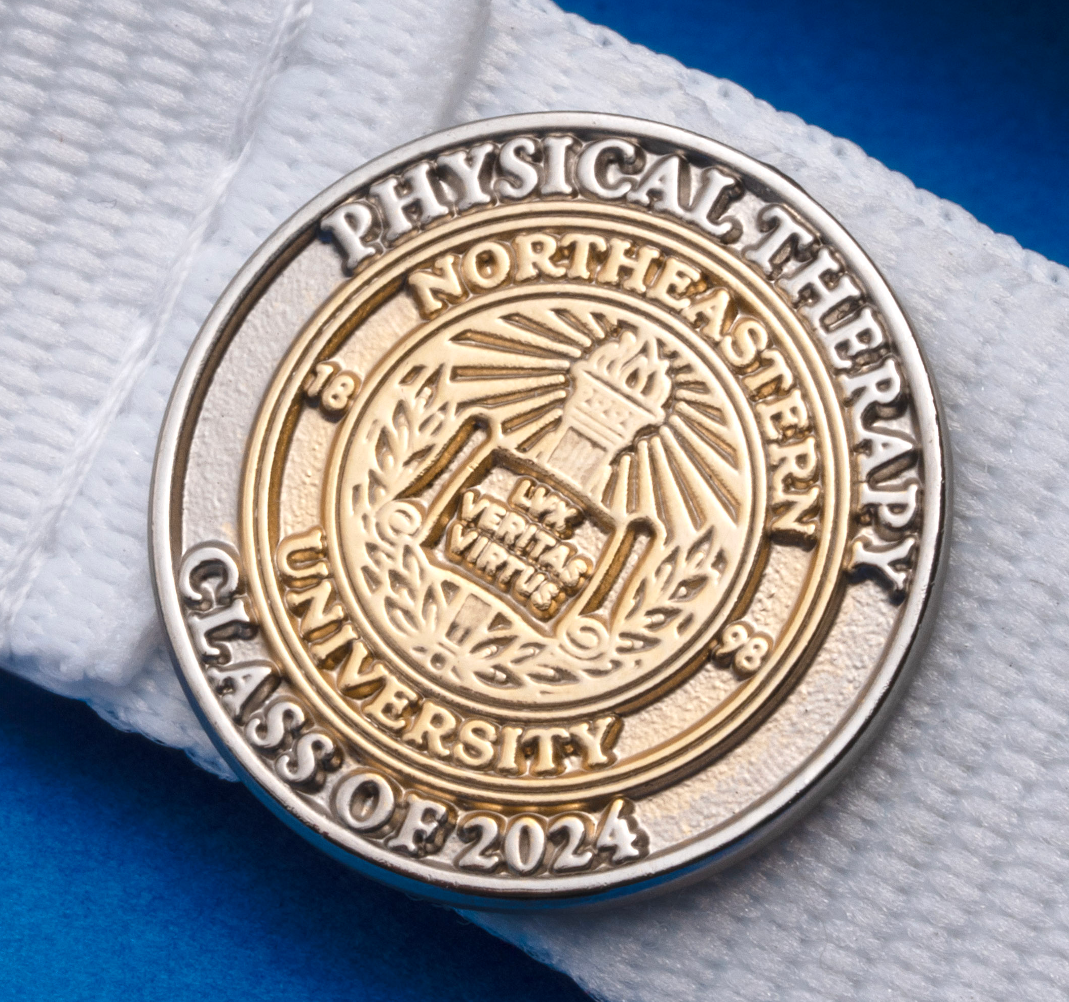Northeastern University Physical Therapy Class of 2024 round enamel lapel pin attached to a white lanyard over a blue background.