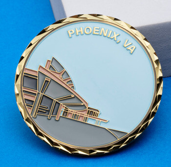 Circular gold challenge coin with a diamond-cut edge featuring a modern building illustration and the text Phoenix, VA.