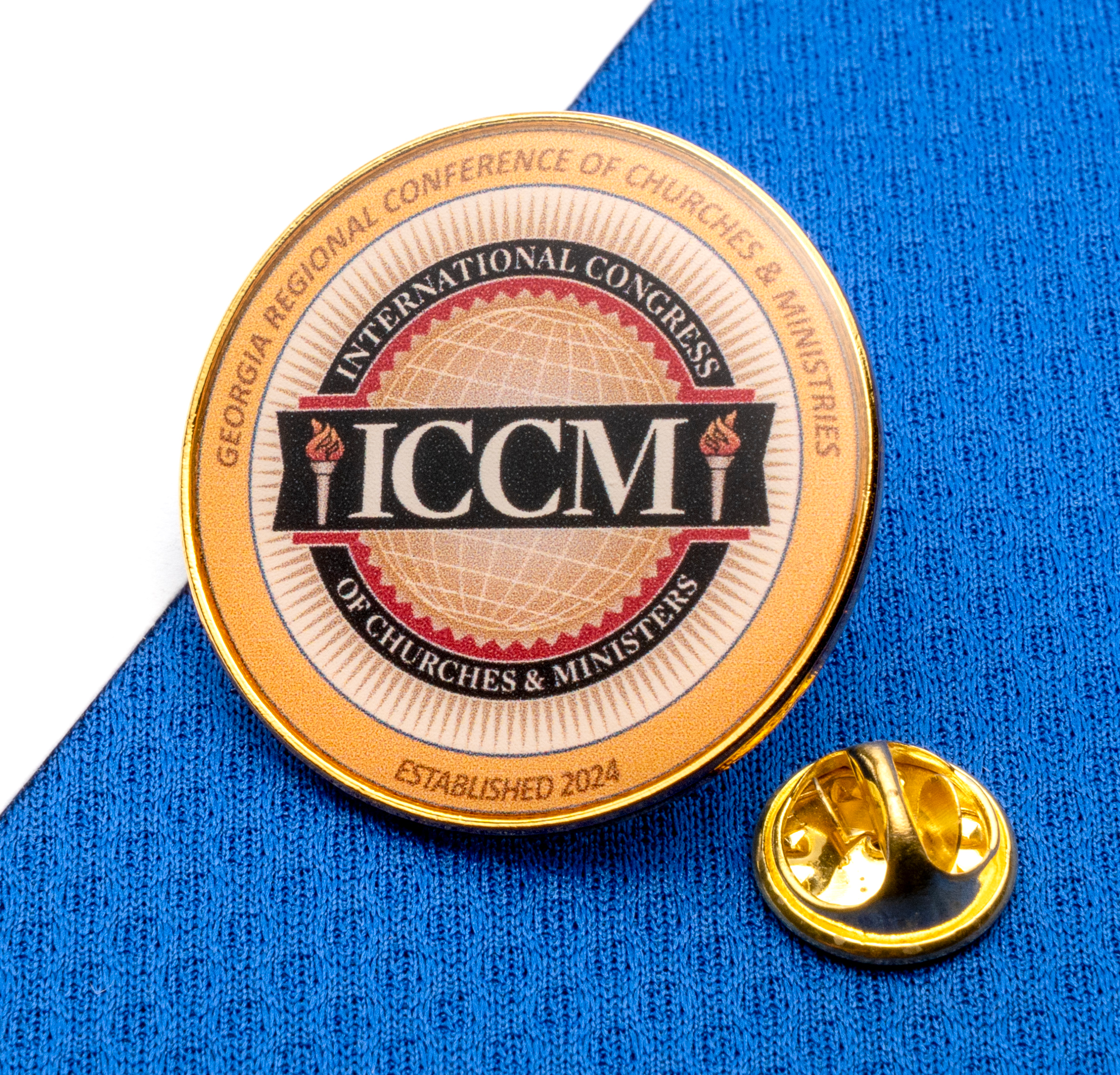 Gold circular lapel pin with ICCM logo and International Congress of Churches & Ministers text on a blue textured background.