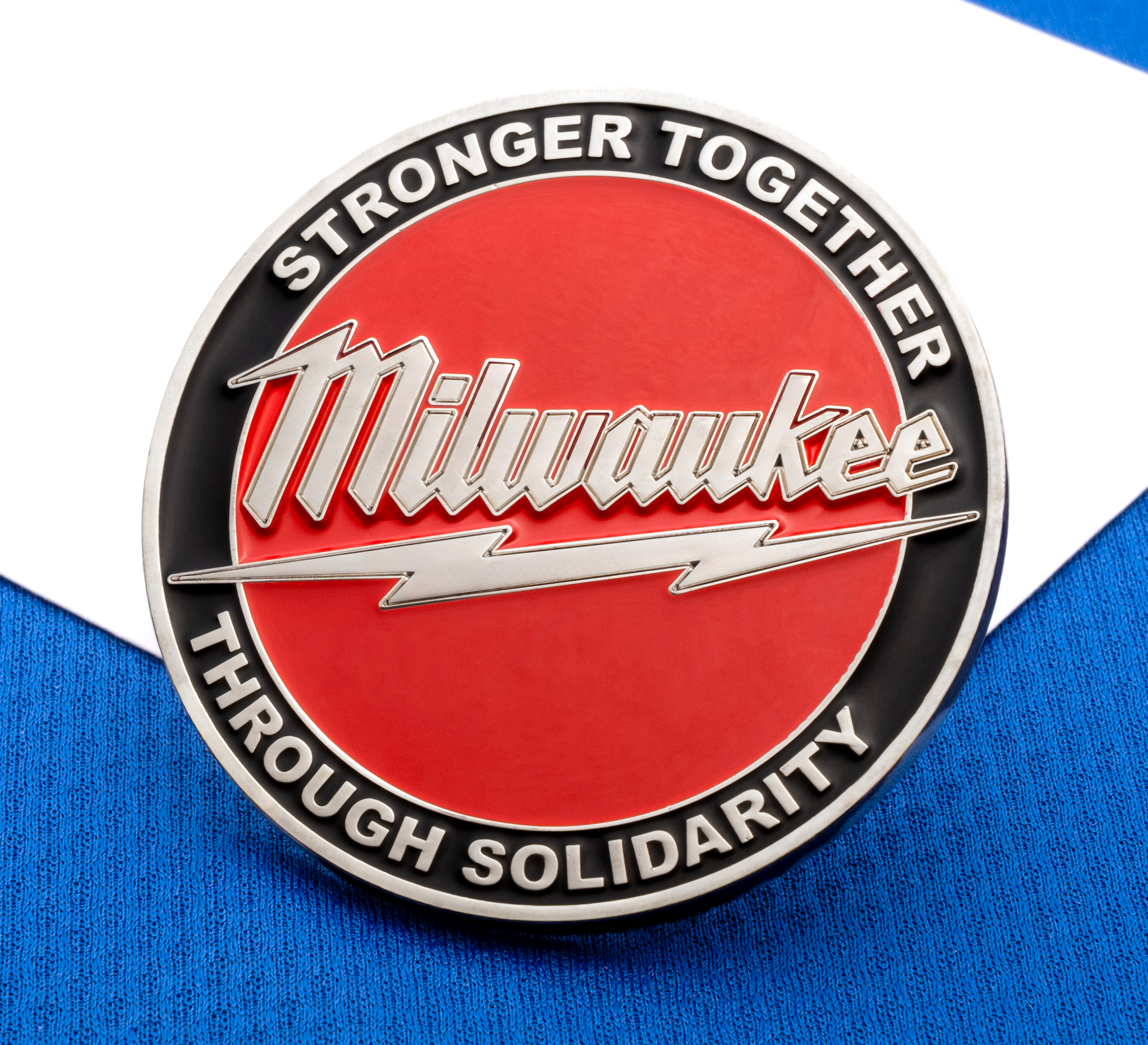 Circular Milwaukee lapel pin with red and black enamel, featuring the text Stronger Together Through Solidarity and a lightning bolt design.