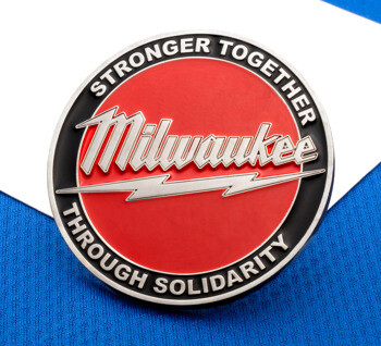 Circular Milwaukee lapel pin with red and black enamel, featuring the text Stronger Together Through Solidarity and a lightning bolt design.