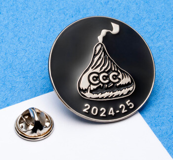 Round black enamel lapel pin featuring a silver chocolate kiss icon with CCC text and the date 2024-25.