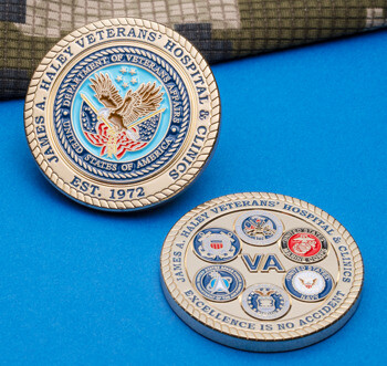 Front and back of a gold challenge coin for James A. Haley Veterans' Hospital & Clinics featuring the VA seal and military branch emblems on a blue background.