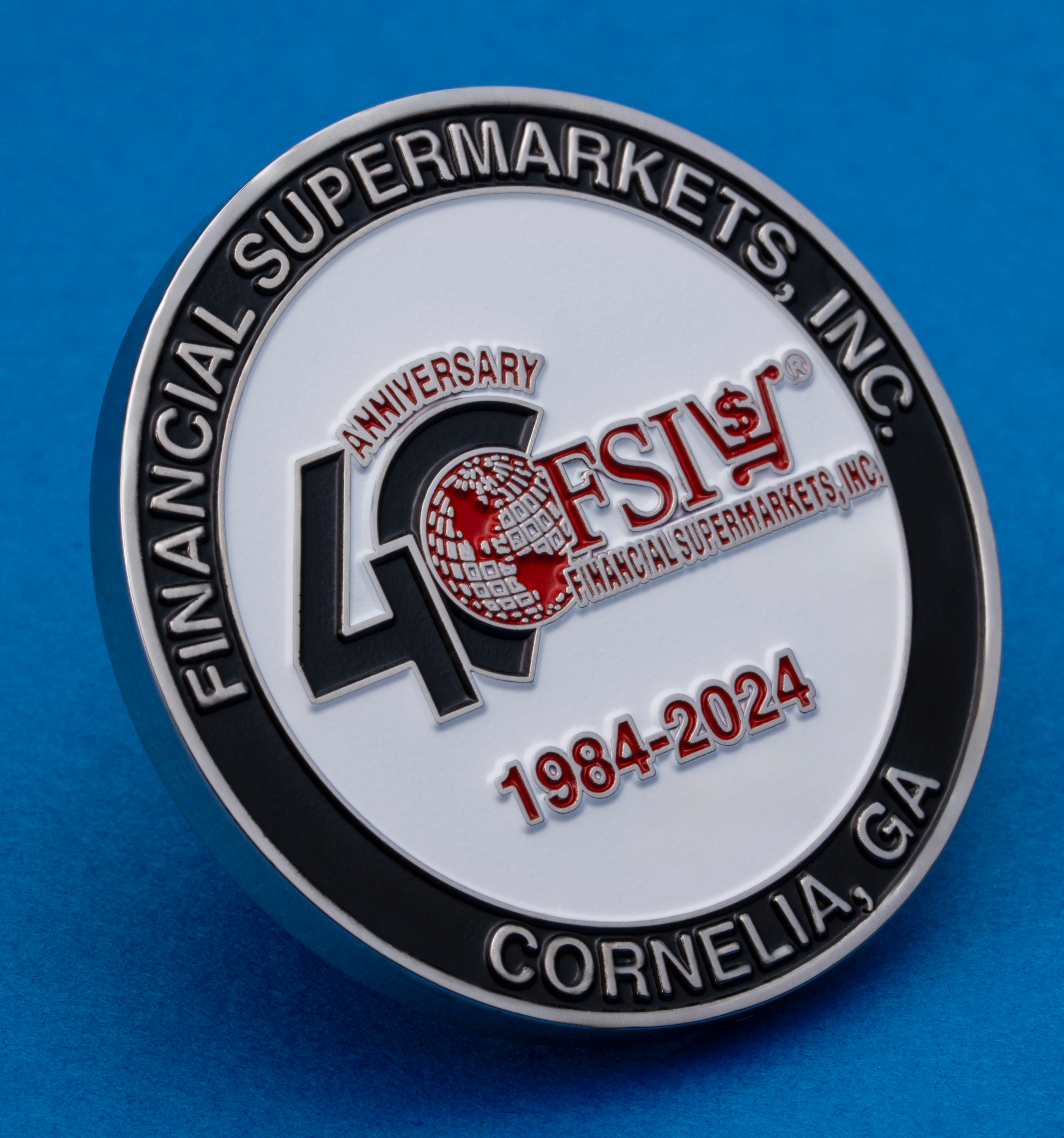 Circular 40th anniversary challenge coin for Financial Supermarkets, Inc. featuring 1984-2024 dates and Cornelia, GA text on a blue background.