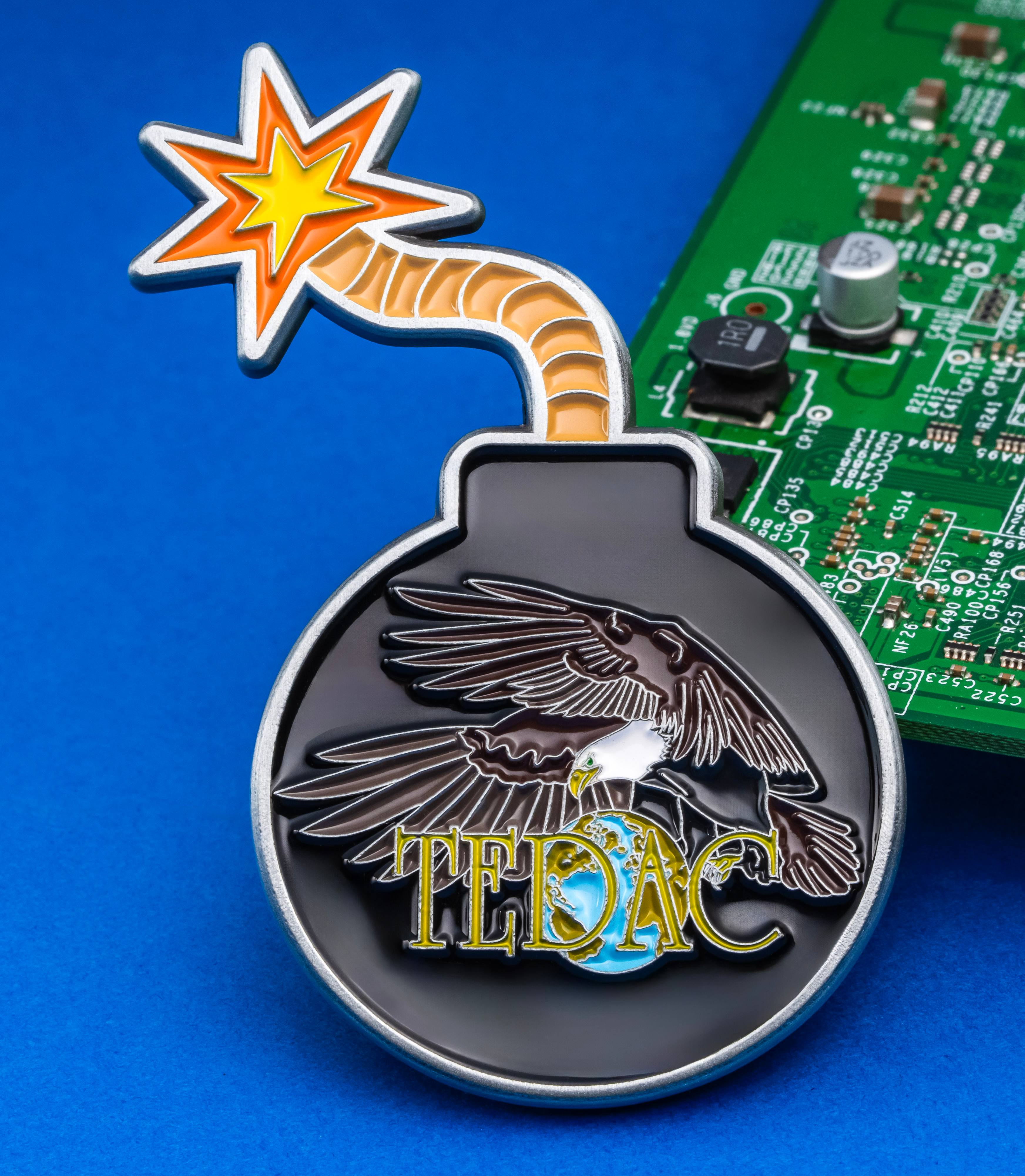 Enamel bomb-shaped pin with an eagle, globe, and TEDAC text next to a green circuit board.